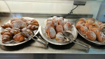 Una teca con tre vassoi di pasticceria, tra cui croissant e altri dolci lievitati, spolverati di zucchero a velo.