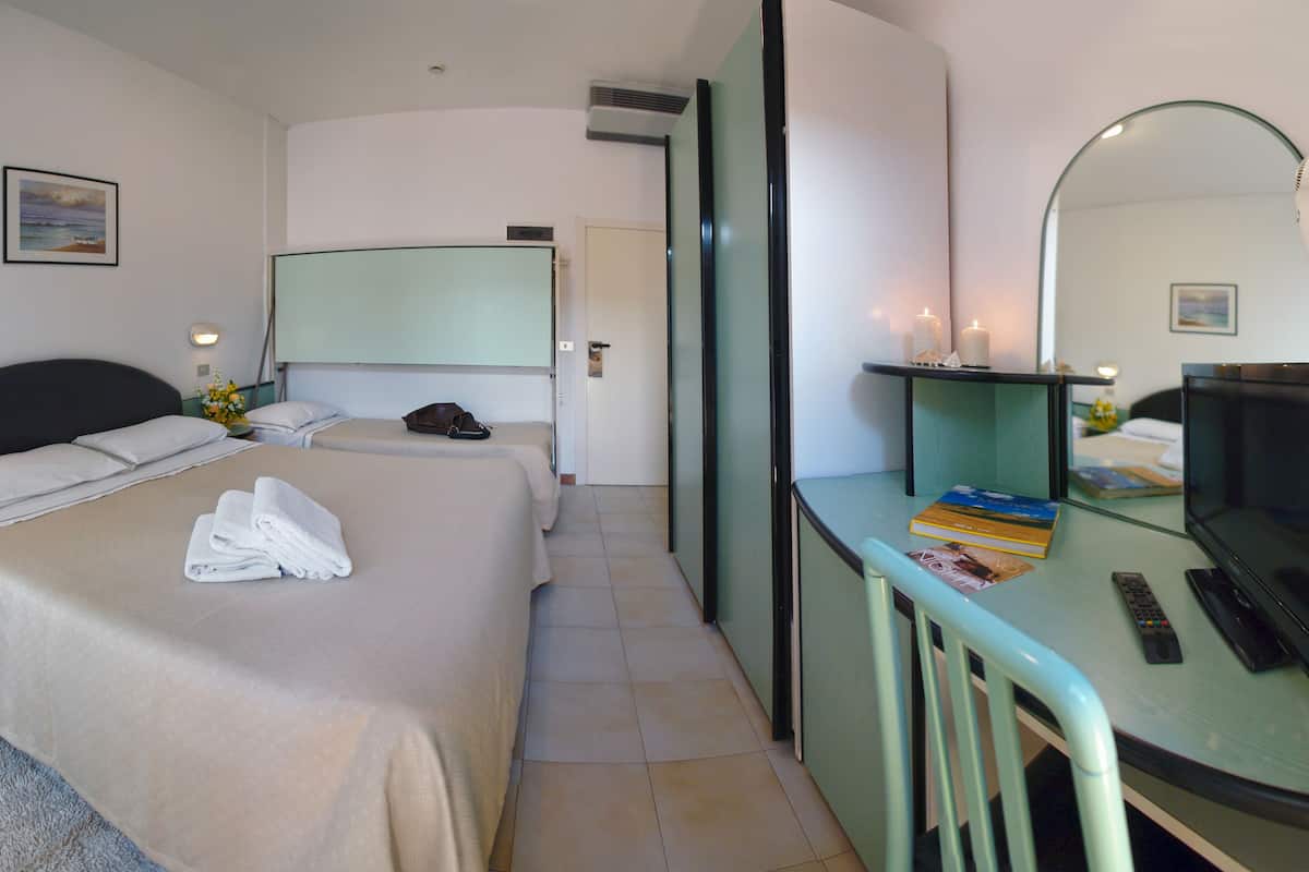 Ein Hotelzimmer mit zwei Betten, einem Schreibtisch mit Spiegel, einem Fernseher und einem Fön.
