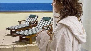 A person in a robe looking out at a beach with two striped lounge chairs. - Hotel Cavalluccio Marino (Gabicce Mare)