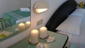 Habitación de hotel con cama, mesita de noche con velas, espejo y un pequeño escritorio con un cuaderno y un folleto.