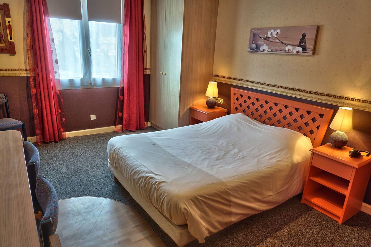 Ein Hotelzimmer mit einem großen Bett, zwei Nachttischen mit Lampen, einem Sessel und einem Fenster mit Vorhängen.
