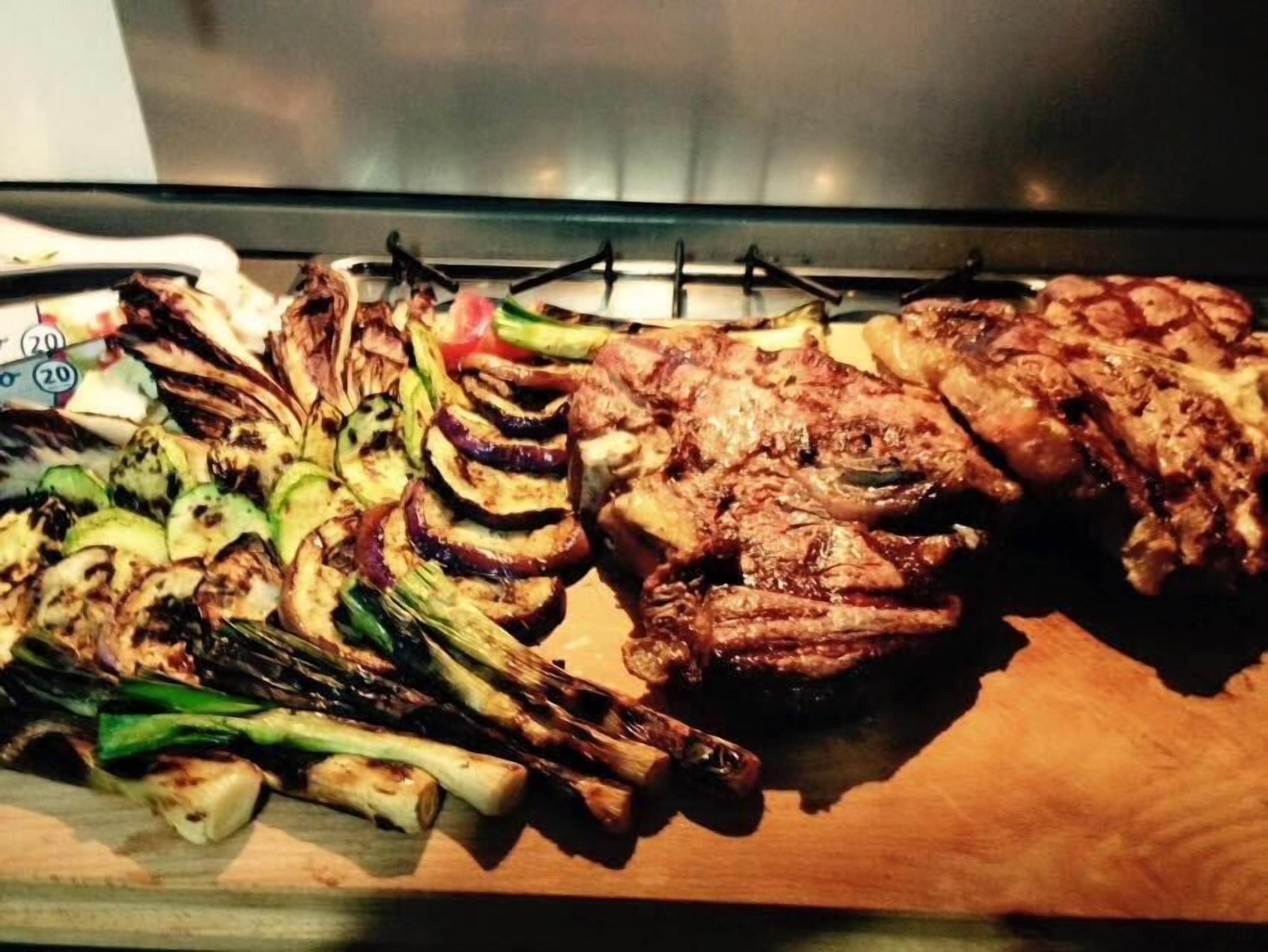 A variety of grilled meats and vegetables on a wooden board.