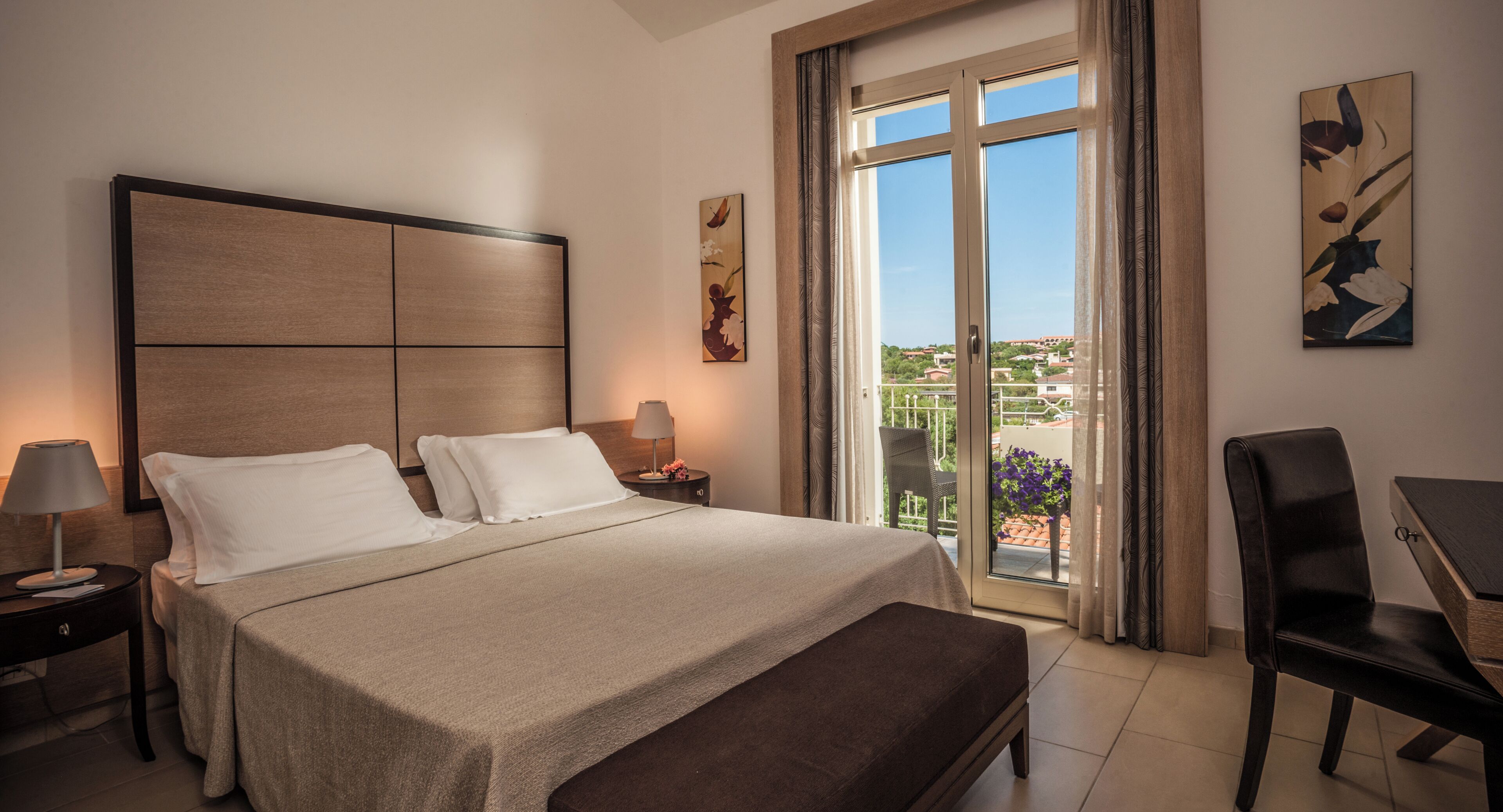 Habitación de hotel con cama, escritorio, silla, mesita de noche y ventana con vistas.
