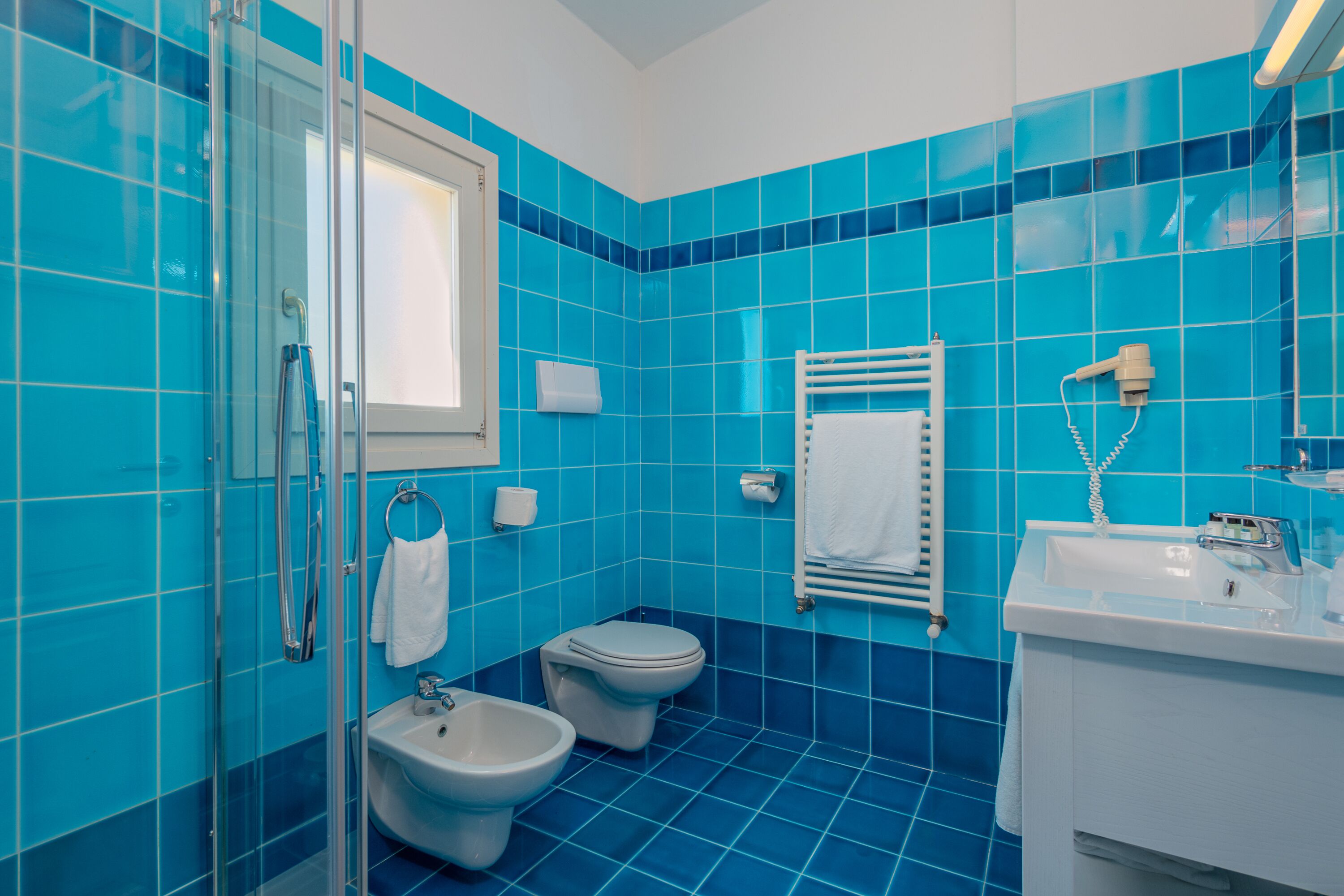 A bathroom with blue tiles, a glass shower enclosure, a sink, and two toilets.