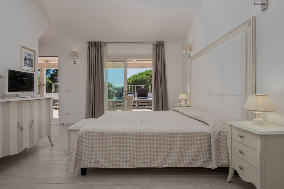 Un dormitorio con cama, mesita de noche, lámpara, televisor y vistas al exterior.
