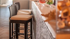 A bar area with a view of the outdoors, featuring a bar counter, stools, and a variety of drinks. - The Pelican Beach Resort & SPA - Adults Only (Olbia)