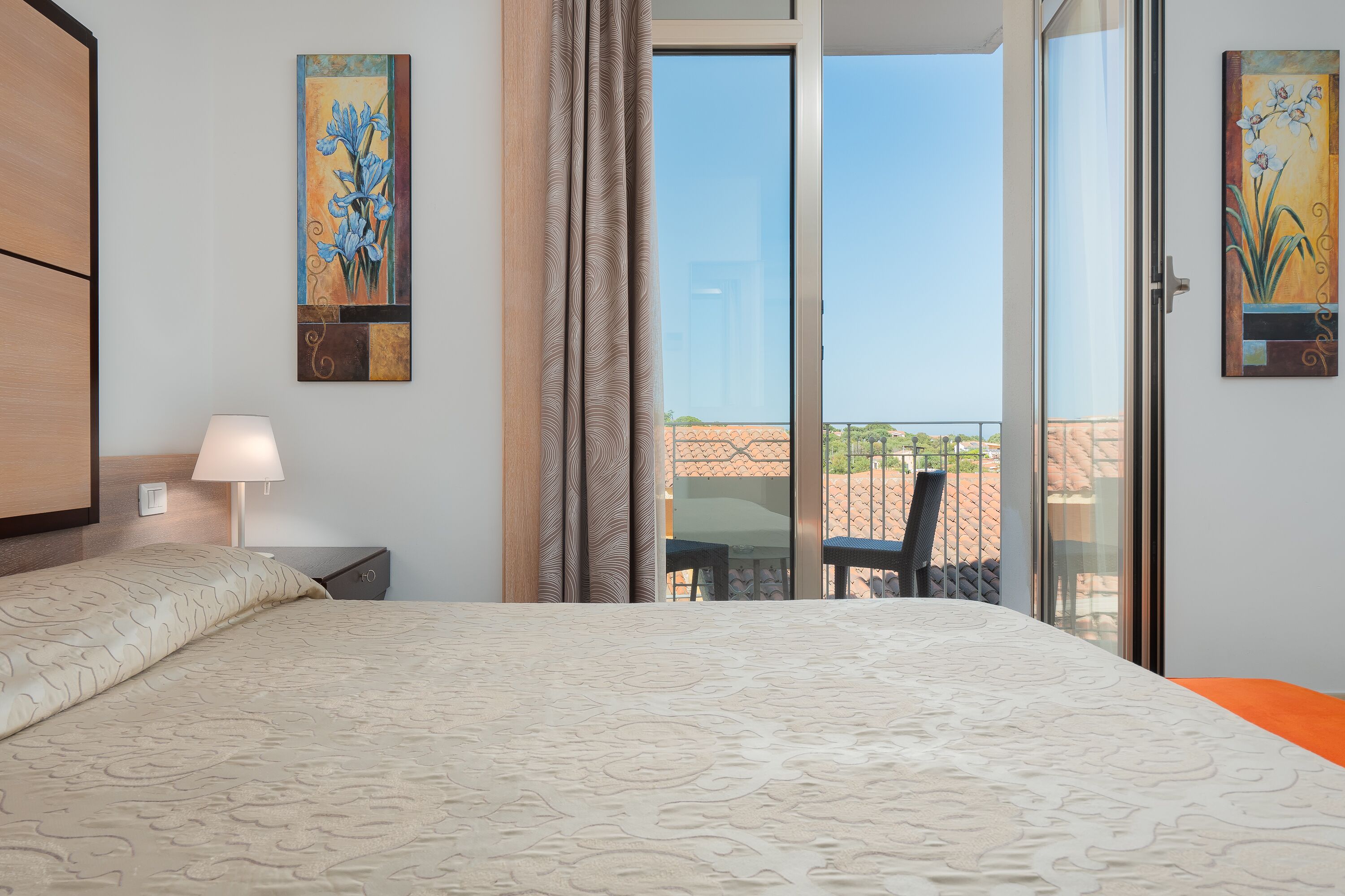A hotel room with a bed, a nightstand, a lamp, and a balcony with a view.