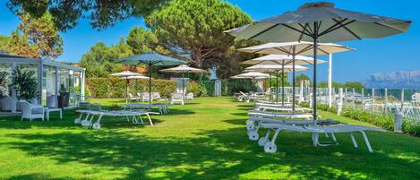 A well-maintained outdoor area with white lounge chairs and umbrellas, a glass-enclosed structure, and a view of the sea.