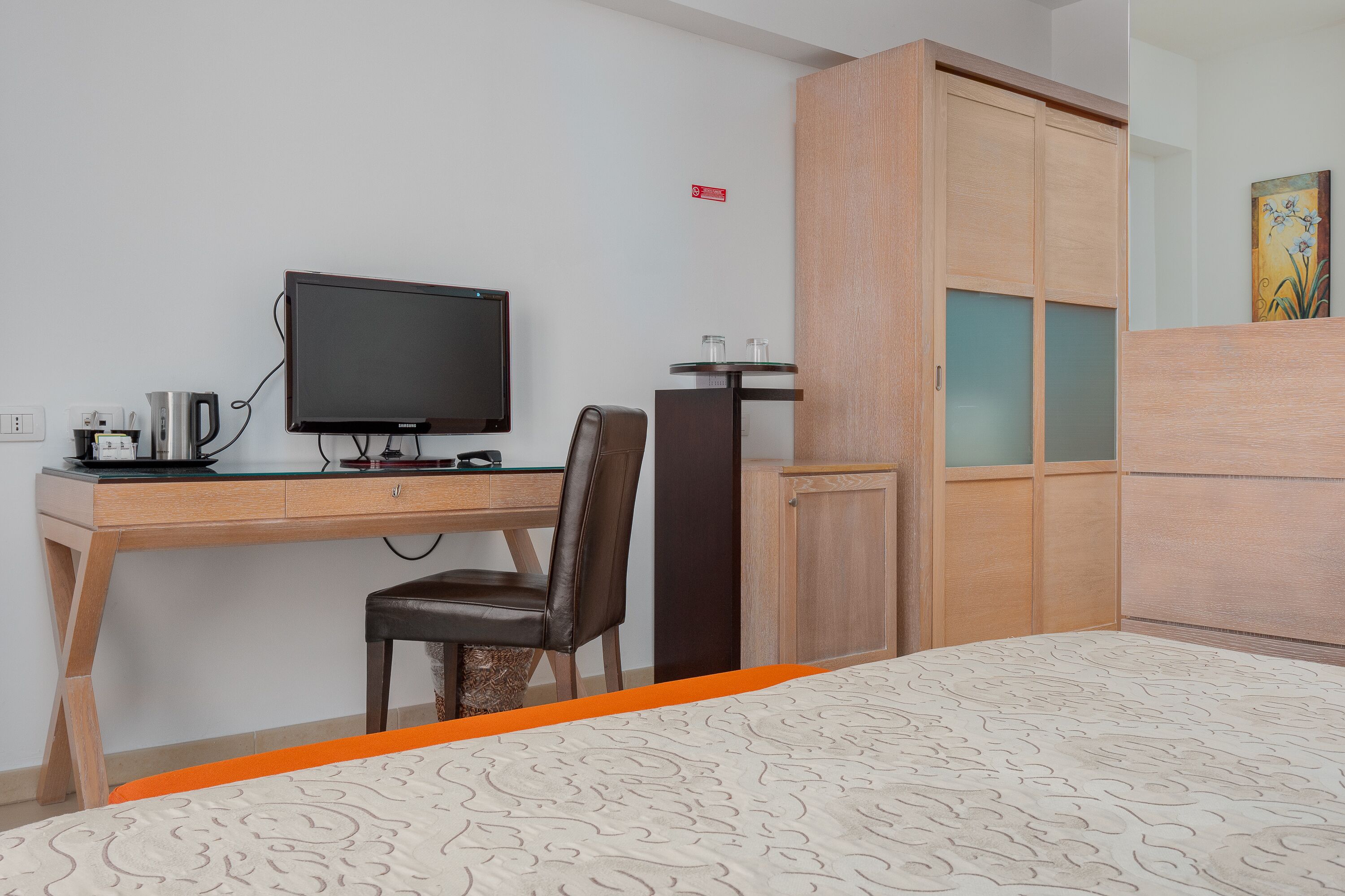 A hotel room with a bed, a desk with a computer, a chair, and a wardrobe.