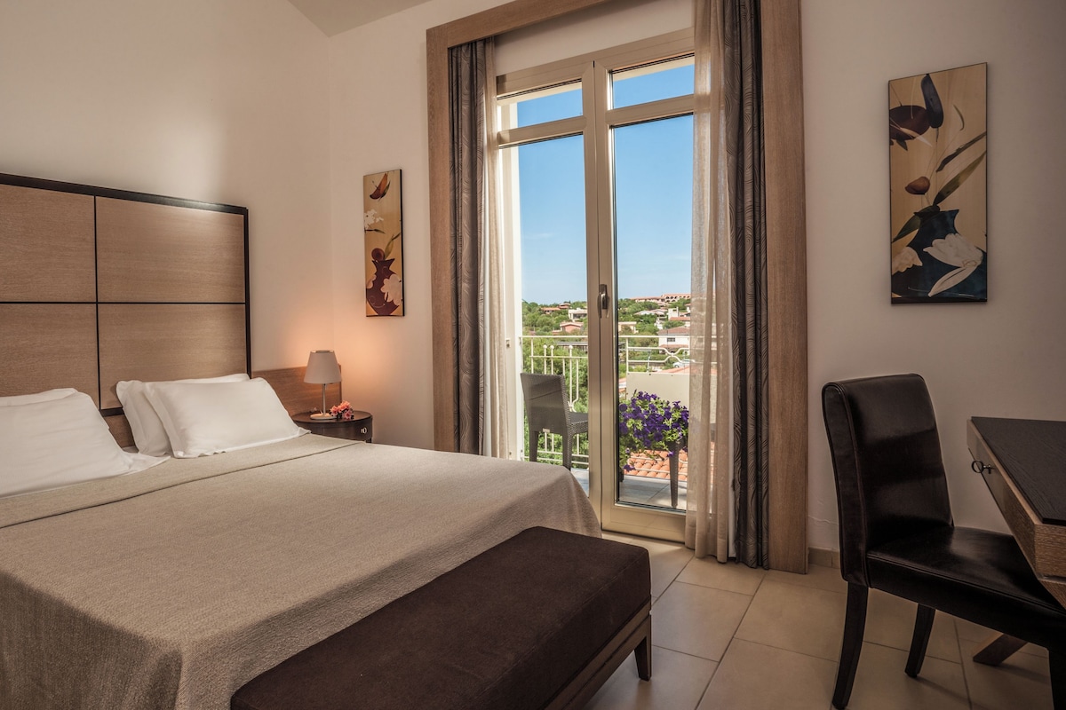 Ein Hotelzimmer mit Bett, Schreibtisch, Stuhl, Nachttisch und einem Fenster mit Aussicht.