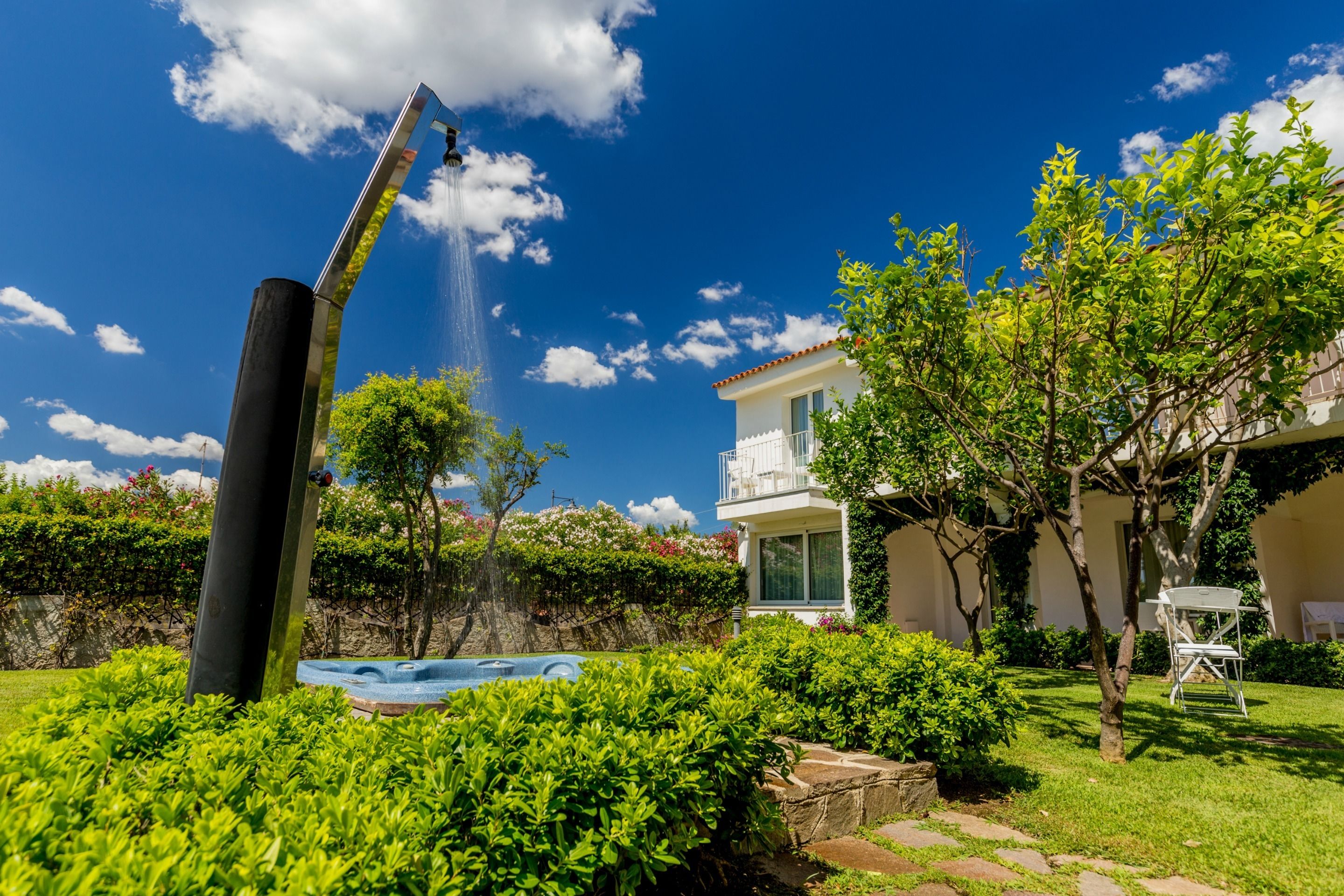 A backyard with a swimming pool, a water fountain, and a white house with a balcony.