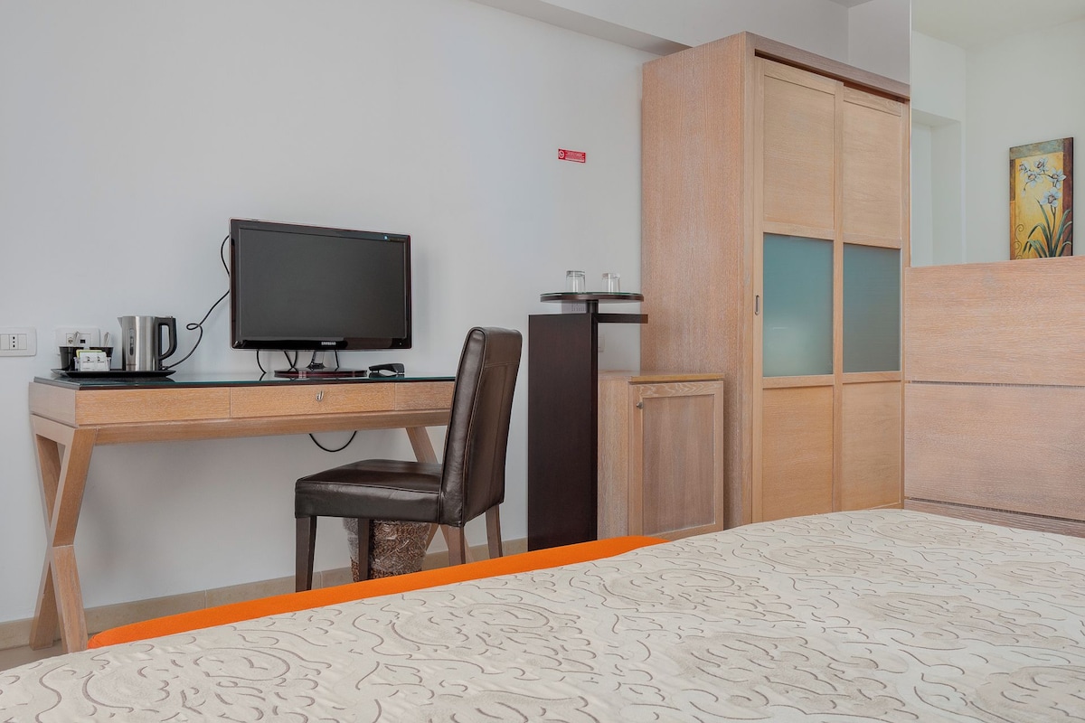 Une chambre d’hôtel équipée d’un bureau, d’une télévision, d’une chaise, d’une armoire et d’un lit.
