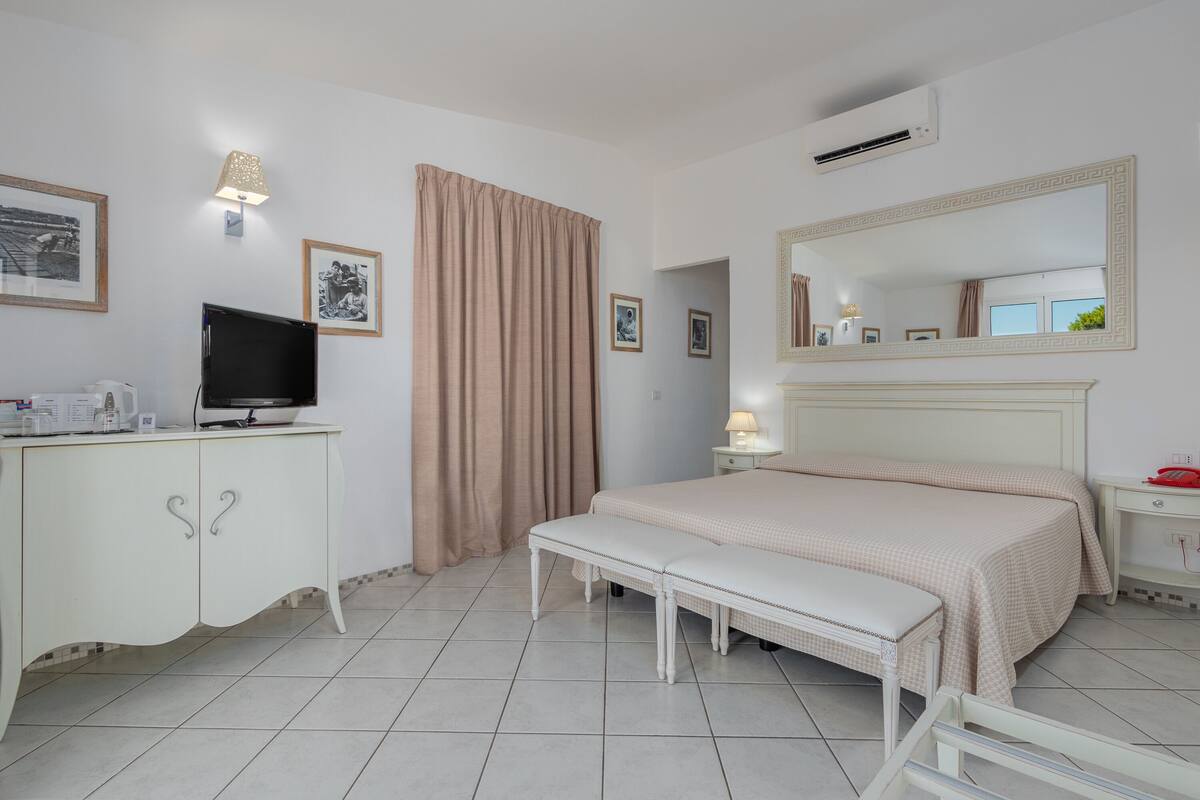 Un dormitorio con cama, una banca, televisor, armario y espejo.