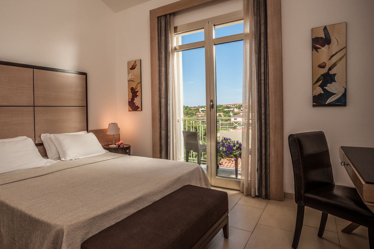 Habitación de hotel con cama, escritorio, silla, mesita de noche y ventana con vistas.