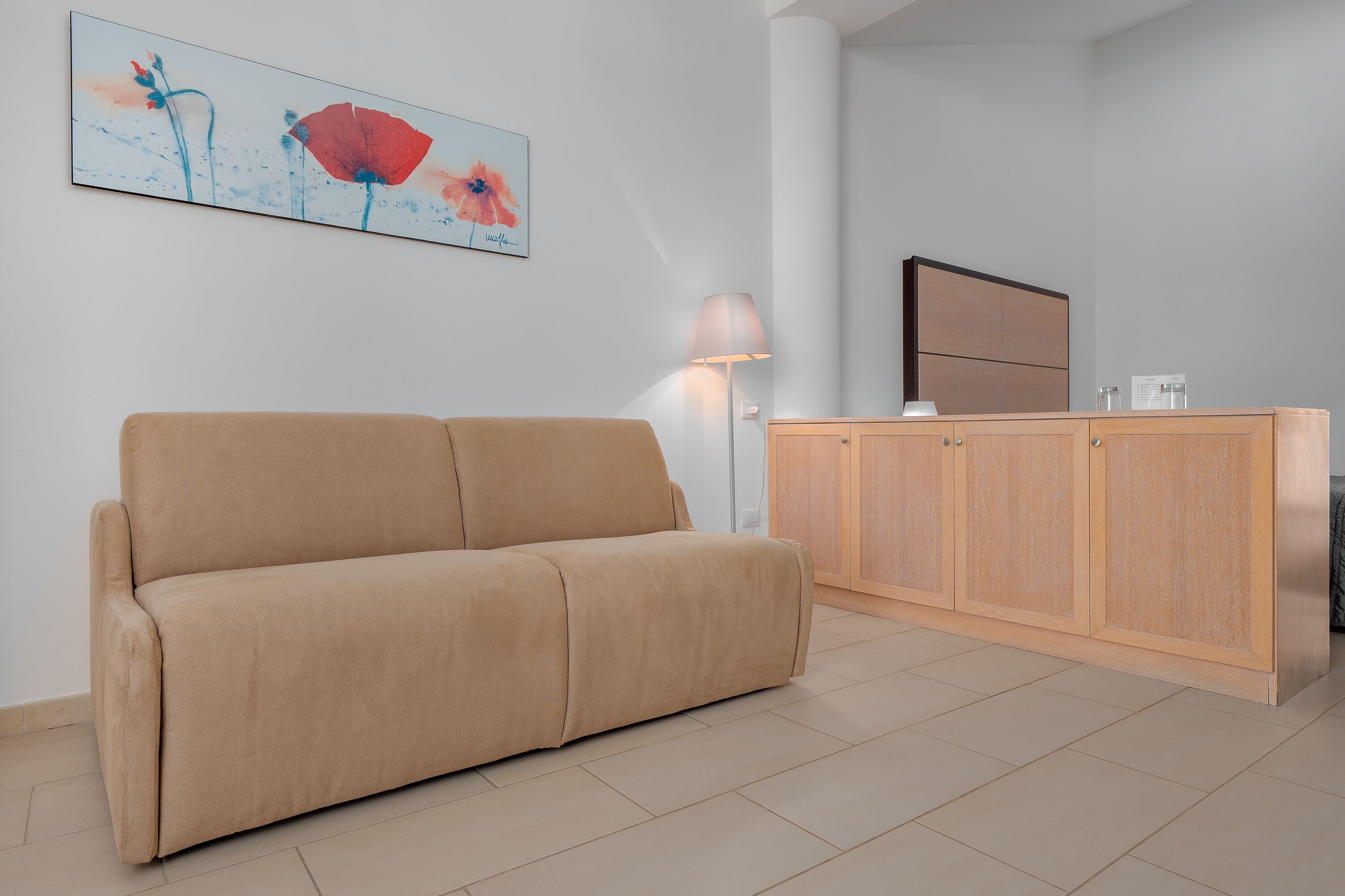 A neutral-toned living area with a beige sofa, a wooden cabinet, and a wall-mounted lamp.