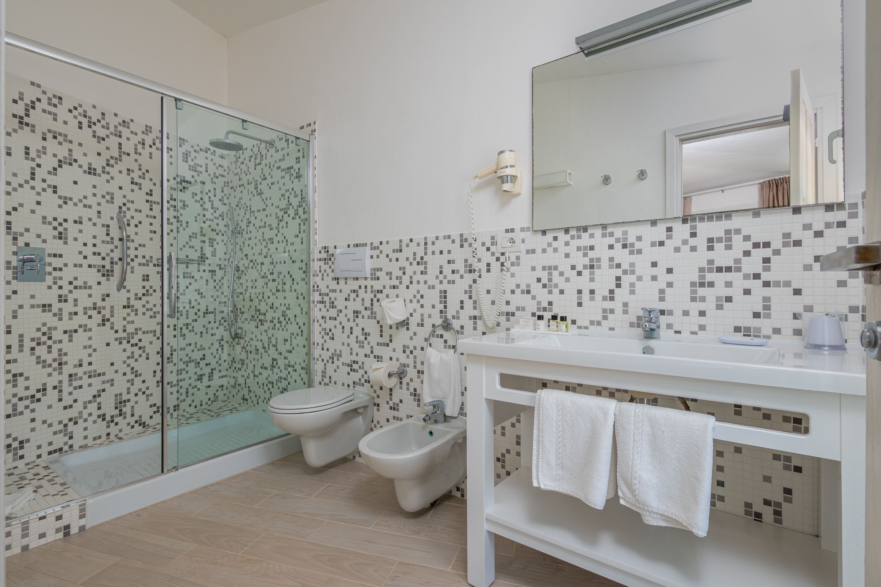Une salle de bain moderne dotée d’une douche à parois de verre, d’un bidet, de toilettes et d’un meuble-lavabo blanc avec un miroir.