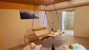 A room with a hanging chair, a table with a bottle of wine, glasses, and towels. - Hotel Garni Brunnthaler (Garmisch-Partenkirchen)
