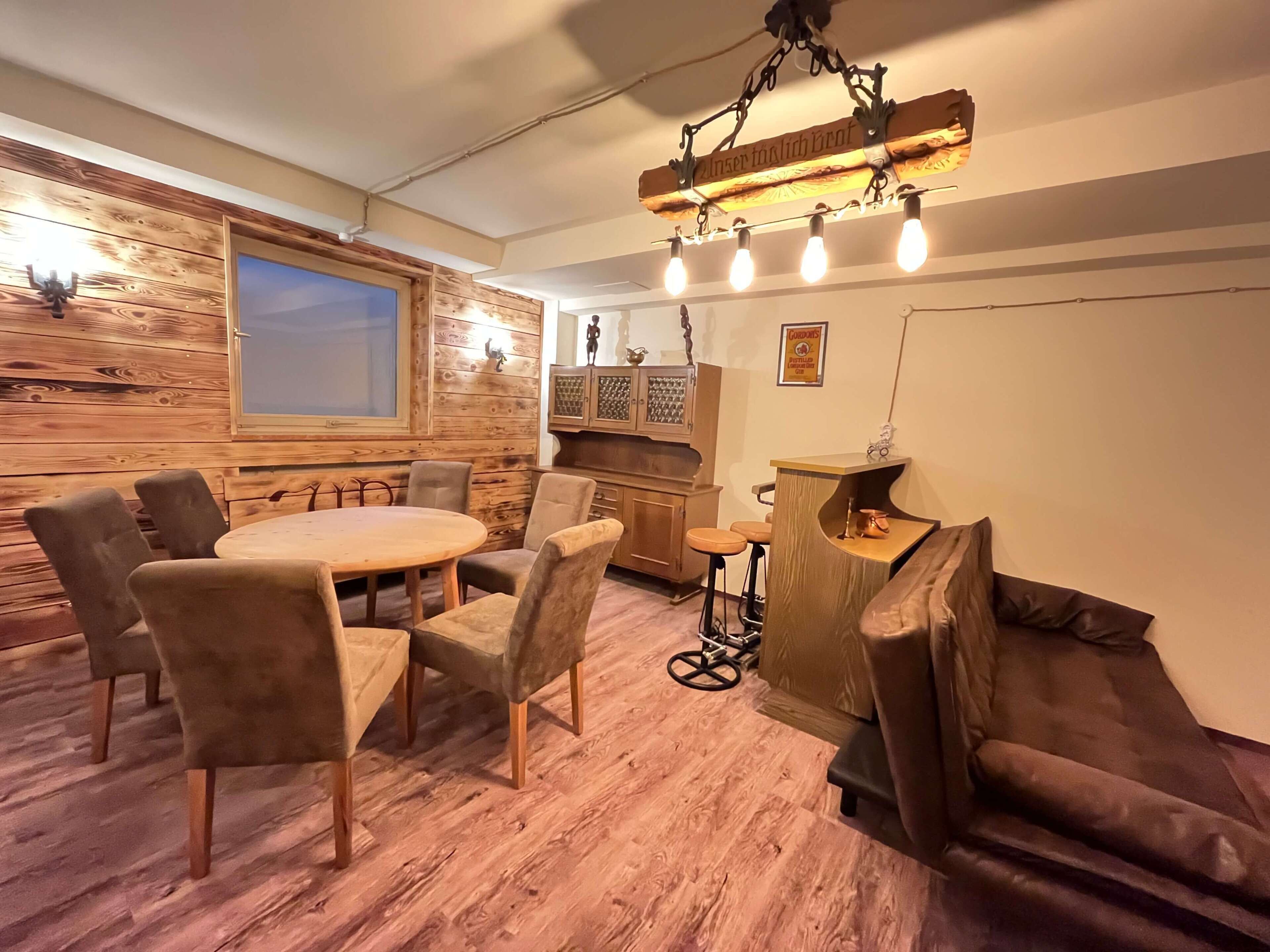 A cozy room with a wooden wall, a round table with chairs, a bar area, and a window.
