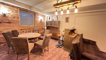 A cozy room with a wooden wall, a round table with chairs, a bar area, and a window.