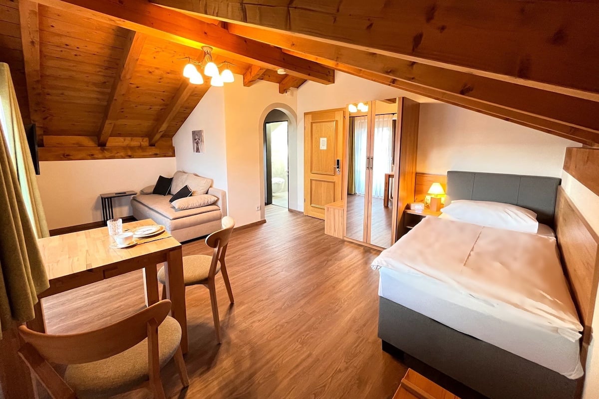 Ett mysigt rum med ett träpanelat tak, en säng, en soffa, ett matbord och en lampa.