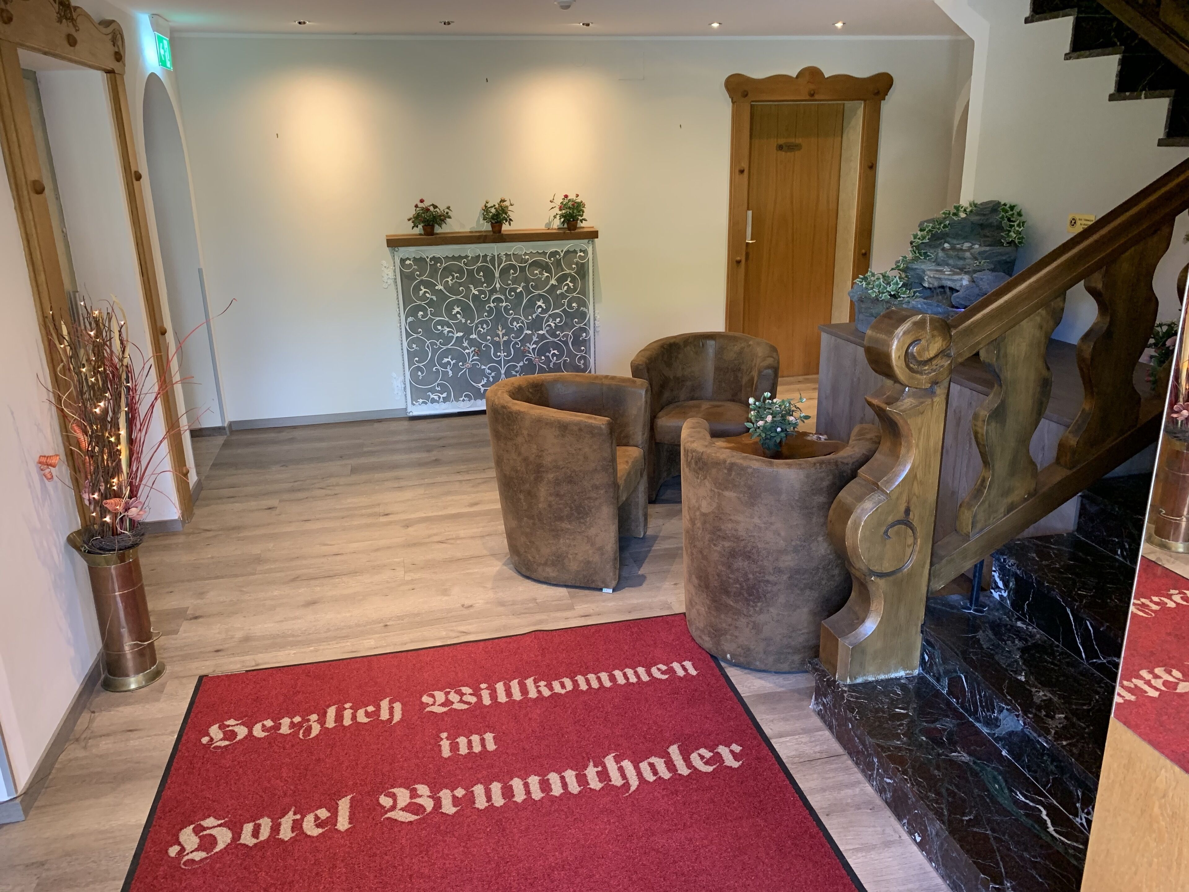 Un hall de hotel con alfombra roja, muebles de madera, un aparador decorativo y una escalera.