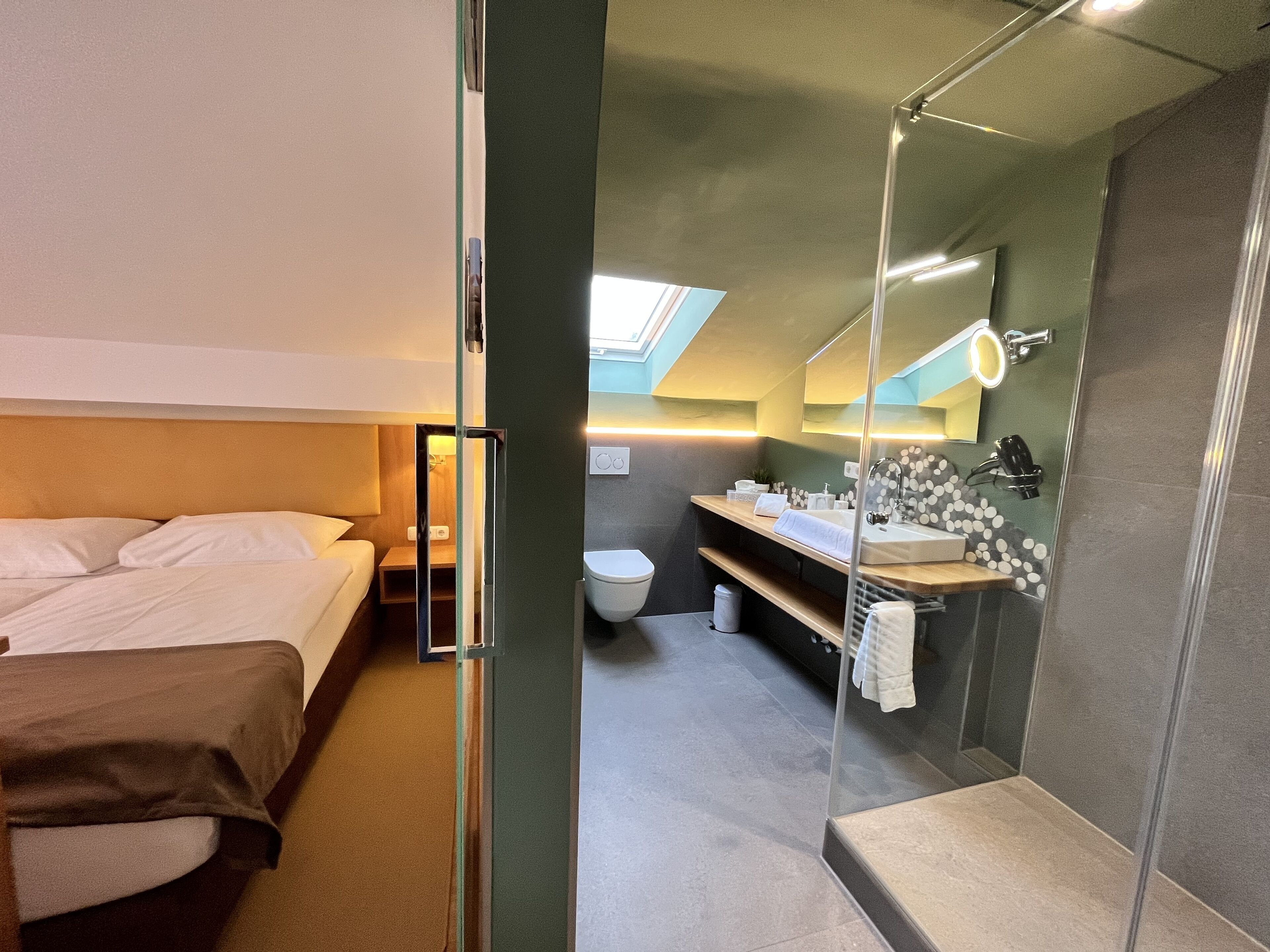 A modern hotel room with a bed, a bathroom with a sink and mirror, and a skylight.
