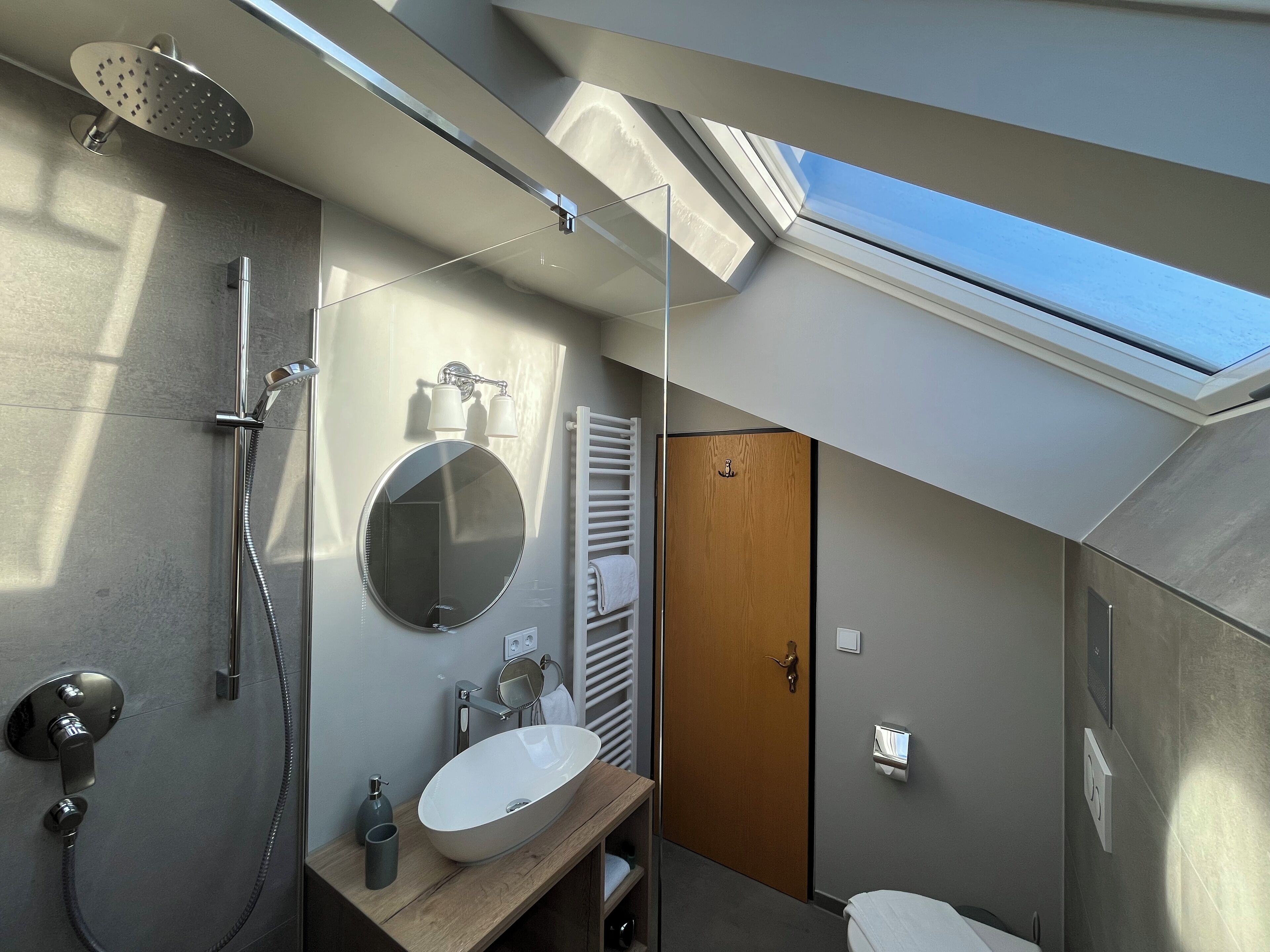 A modern bathroom with a skylight, a round mirror, a sink, and a shower.