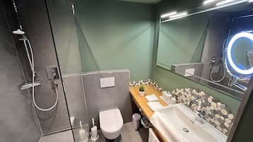A modern bathroom with a glass shower enclosure, a toilet, a sink with a mirror, and a vanity with toiletries.