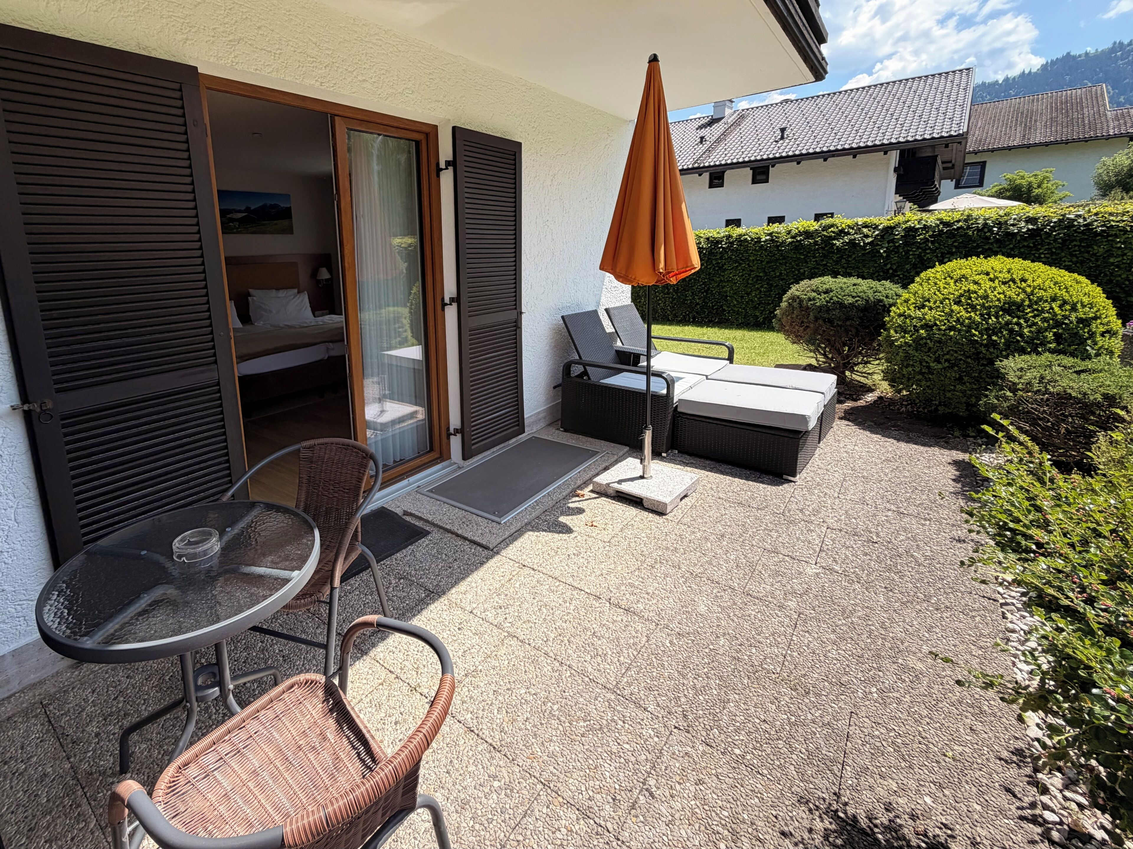 A patio with outdoor furniture, a glass door leading to a room, and a view of a house in the background.