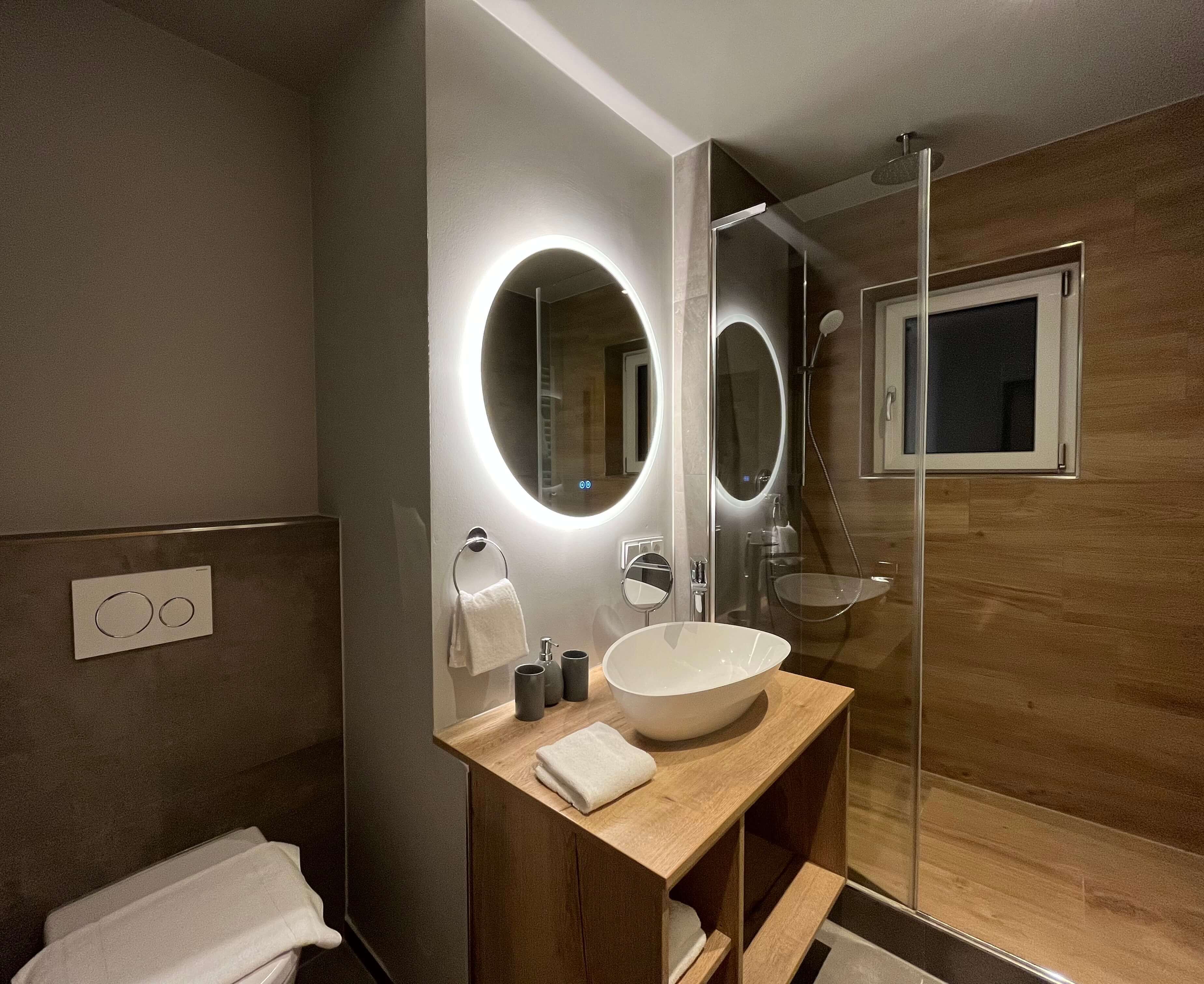 A modern bathroom with a large mirror, a wooden vanity, a white sink, and a glass shower enclosure.