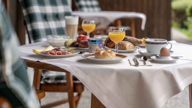 A breakfast table with plates of food, glasses of orange juice, and a cup of coffee. - Hotel Garni Brunnthaler (Garmisch-Partenkirchen)