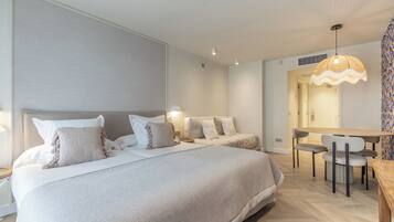 A modern bedroom with two beds, a dining area, and a bathroom visible through an open door.