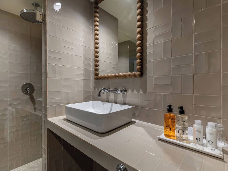 Un baño moderno con lavamanos blanco, espejo con marco de madera y estante con artículos de aseo.