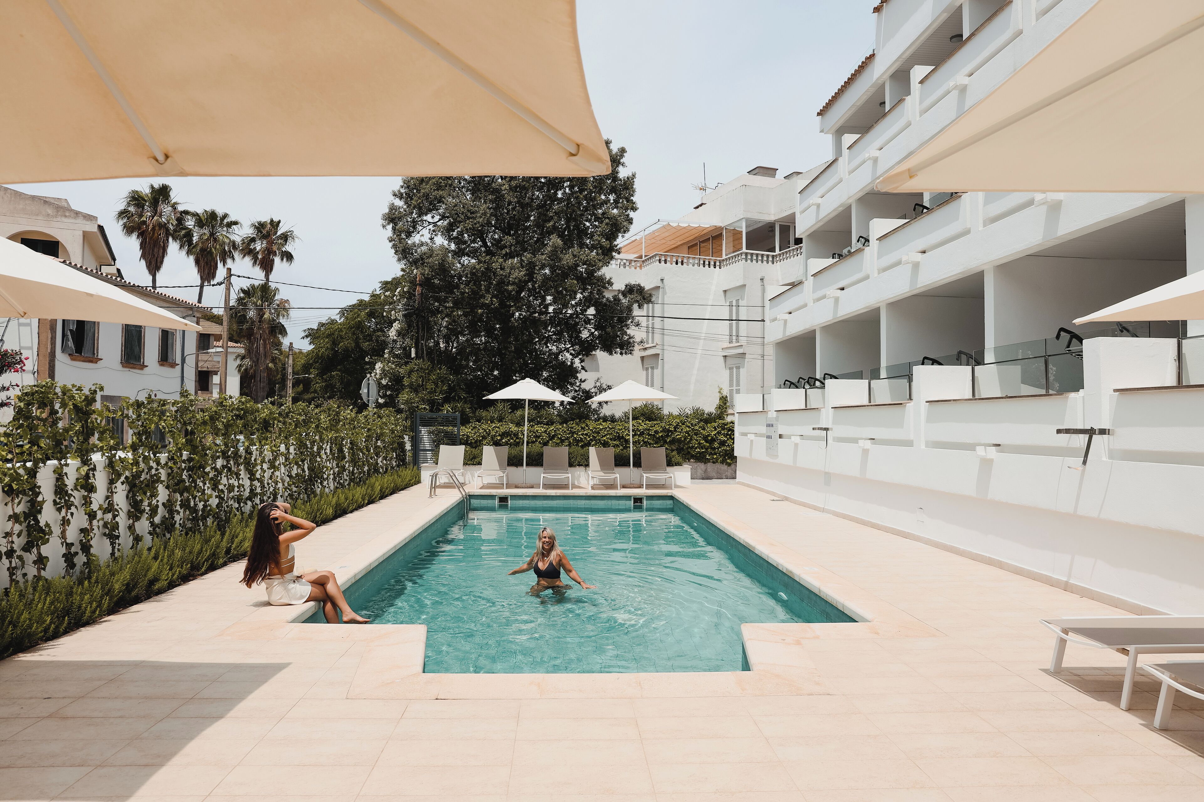 A swimming pool area with lounge chairs and umbrellas, surrounded by buildings and greenery.