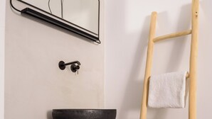 Un baño con un banco de madera, un lavabo negro, una toalla en una escalera de madera, un espejo fijado a la pared y un perchero.