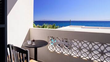 A balcony with a table and chairs, overlooking a clear blue sea and distant mountains.
