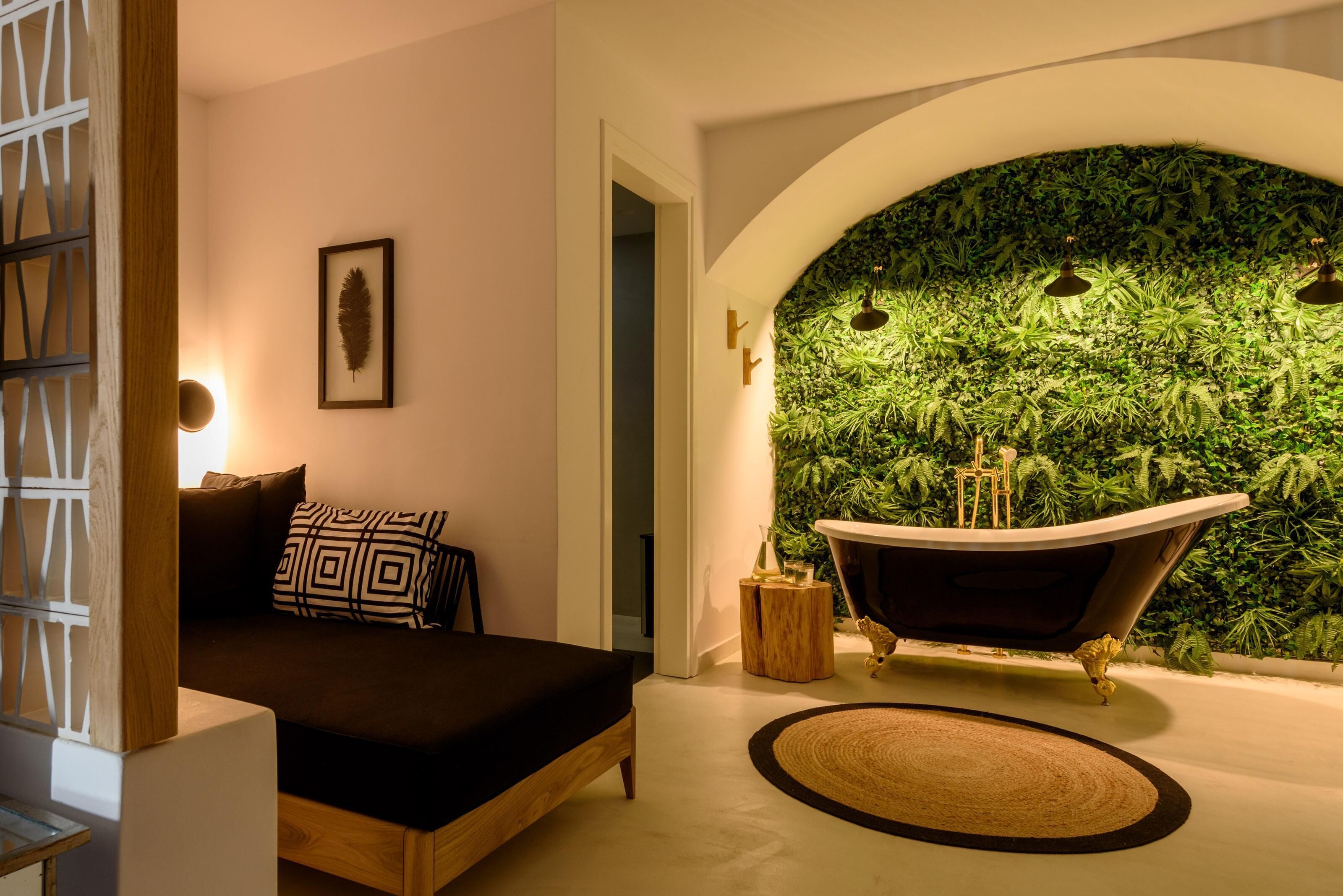 A modern bedroom with a black sofa, a framed leaf artwork, a vintage bathtub, and a green wall with plants.