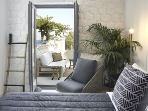 Una habitación con una cama, un sillón gris, una mesita, una escalera y vistas al exterior.