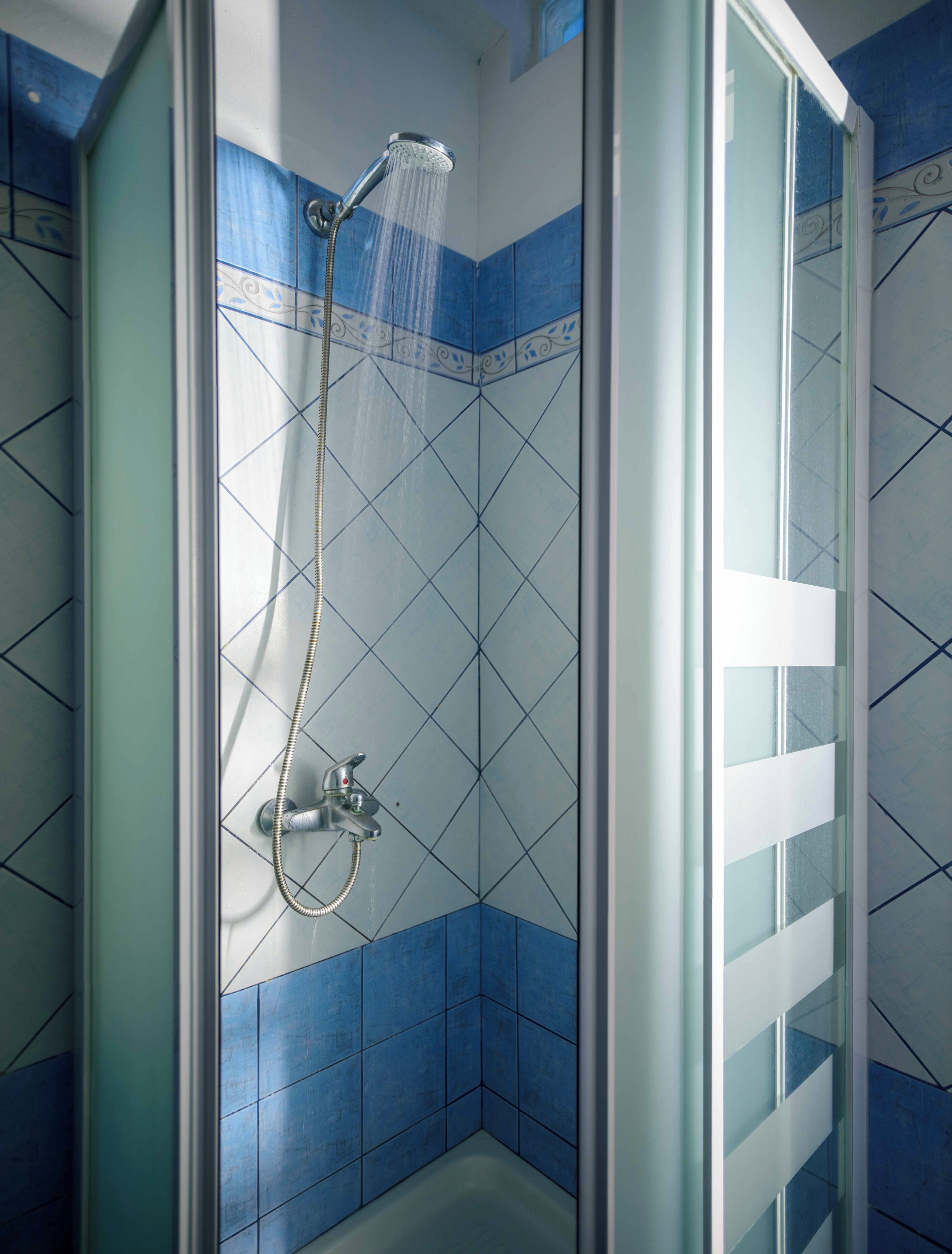 A shower with a glass door, blue tiles, and a handheld showerhead.
