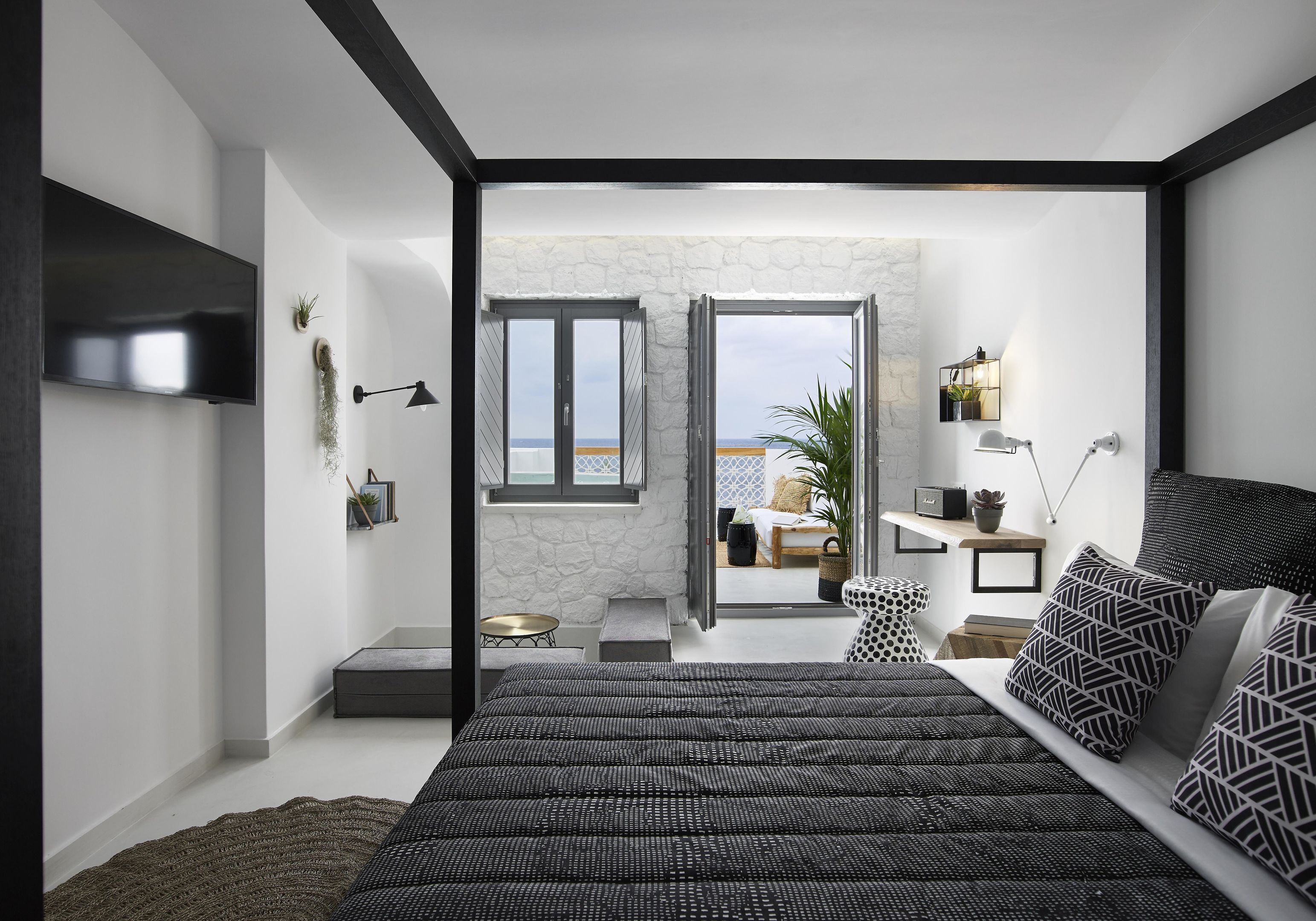 A modern bedroom with a large bed, a TV, and a view to an outdoor balcony.