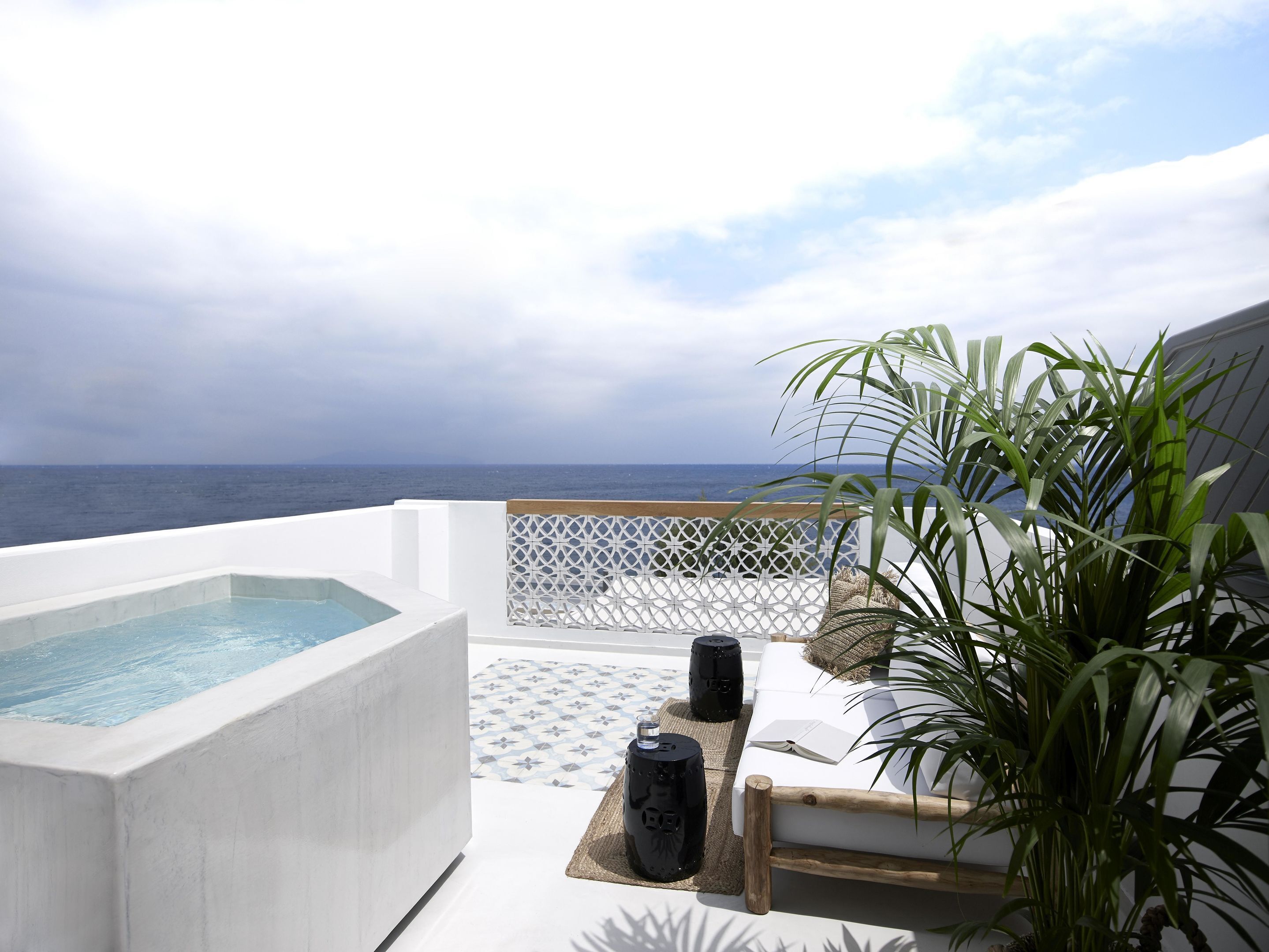 Un espace extérieur moderne, aménagé avec des sièges, une piscine, du mobilier blanc et une vue sur l’océan.