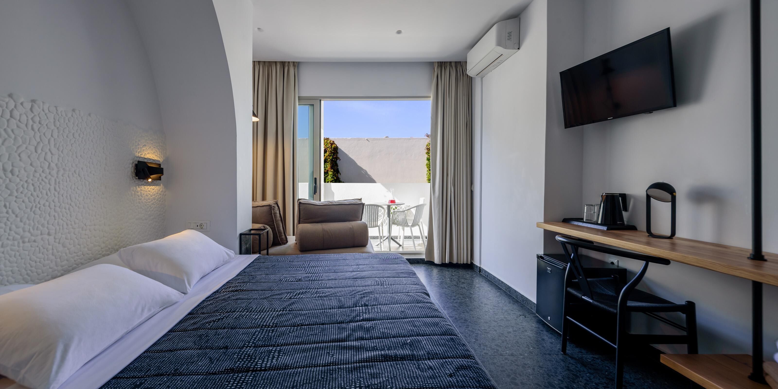 A hotel room with a bed, a desk, a chair, a TV, and a view of the outdoors.