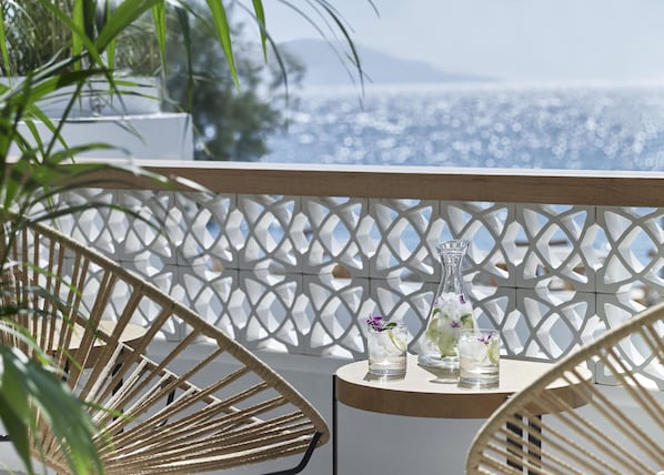 Un balcon agrémenté d’une séparation en treillis blanc, de deux fauteuils en osier et d’une petite table sur laquelle sont posés deux verres d’eau et une bouteille d’eau.