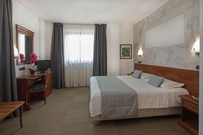 A hotel room with a bed, desk, chair, and a large window with curtains.