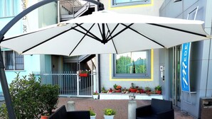 An outdoor seating area with a table and chairs, surrounded by potted plants and a large umbrella. - Medea (Alba)