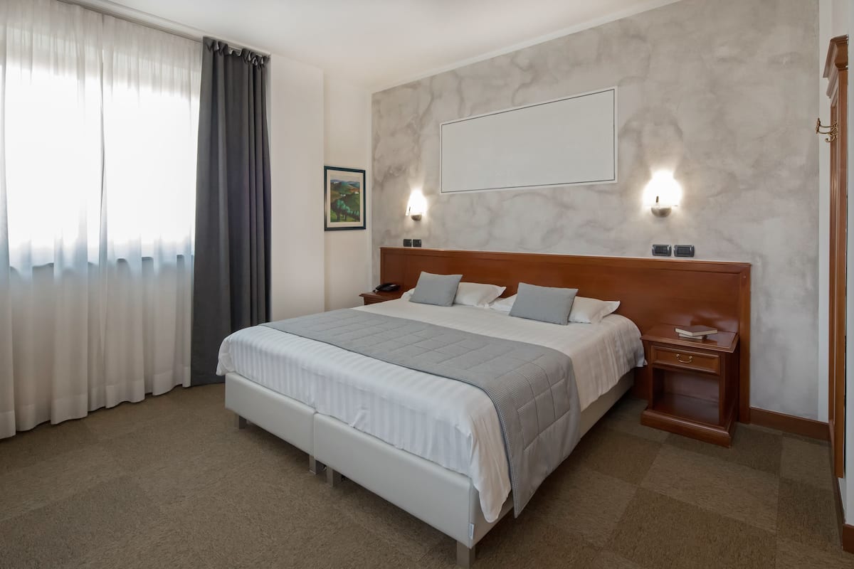 Habitación de hotel ordenada con una cama grande, mesitas de noche y una lámpara fijada a la pared.