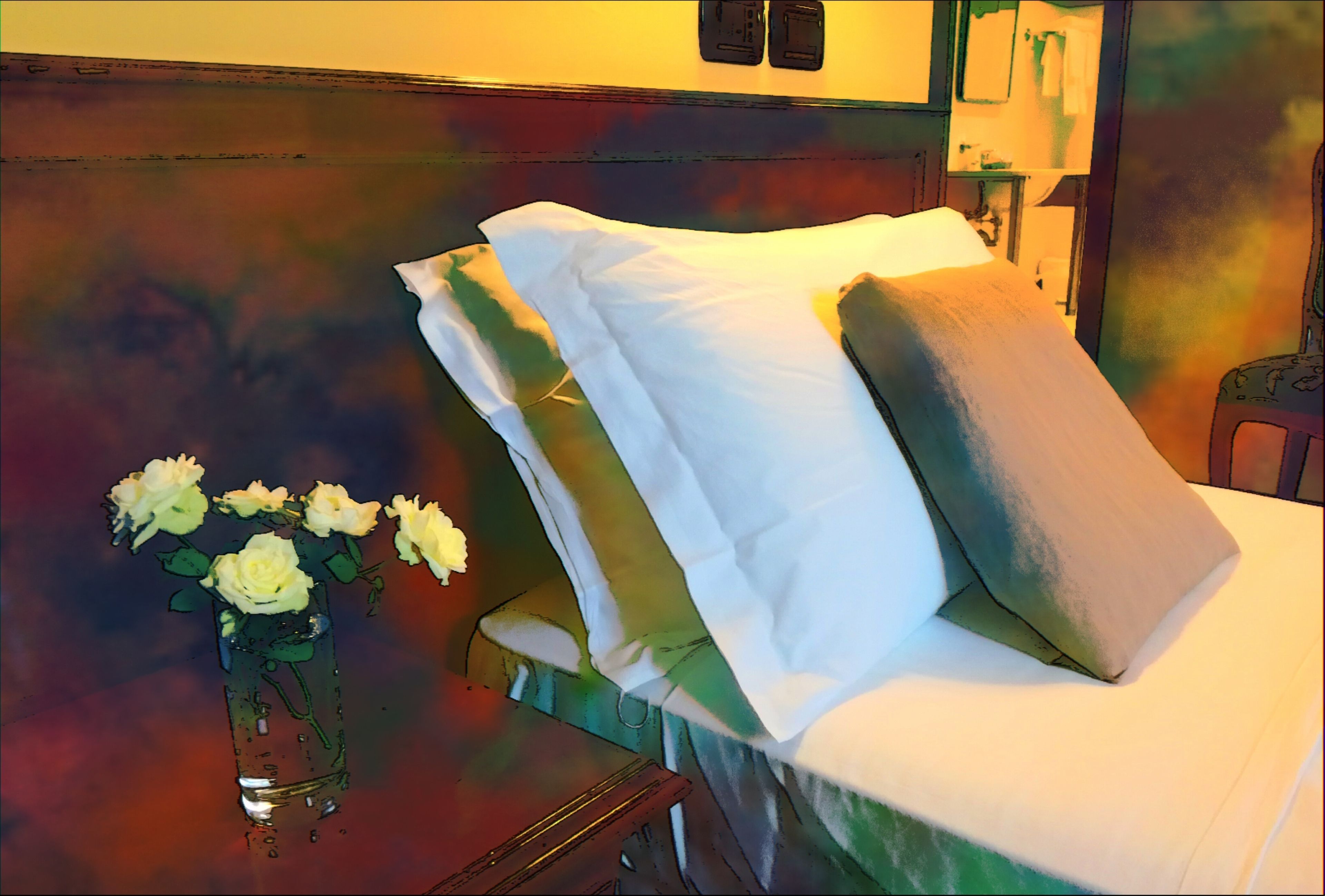 A neatly made bed with white and beige pillows, a small table with a vase of white flowers, and a mirror on the wall.