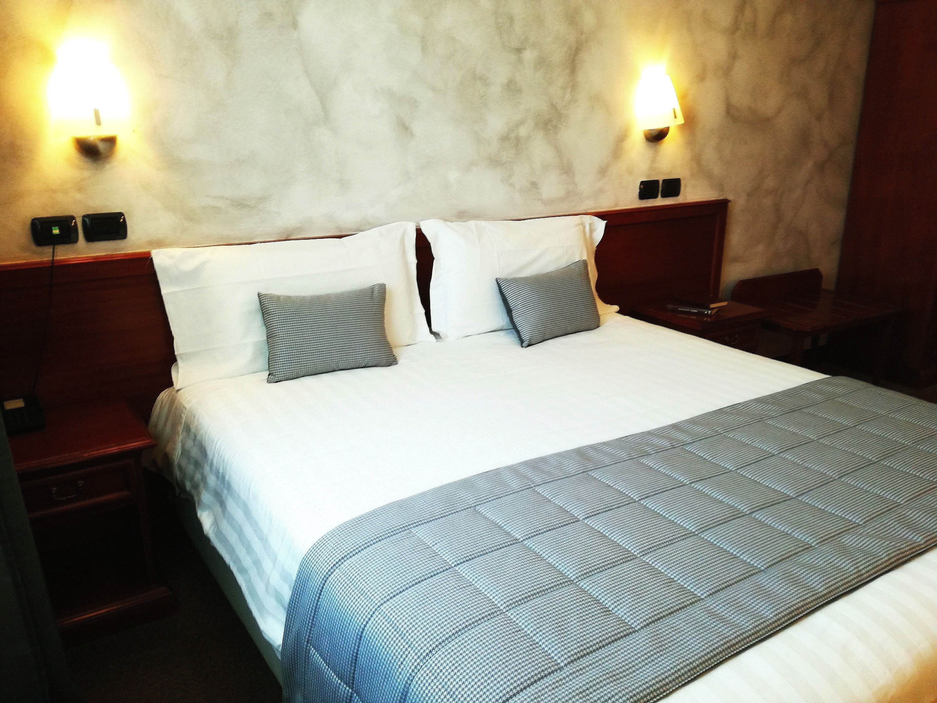 A hotel room with a large bed, two bedside tables, and two wall-mounted lamps.