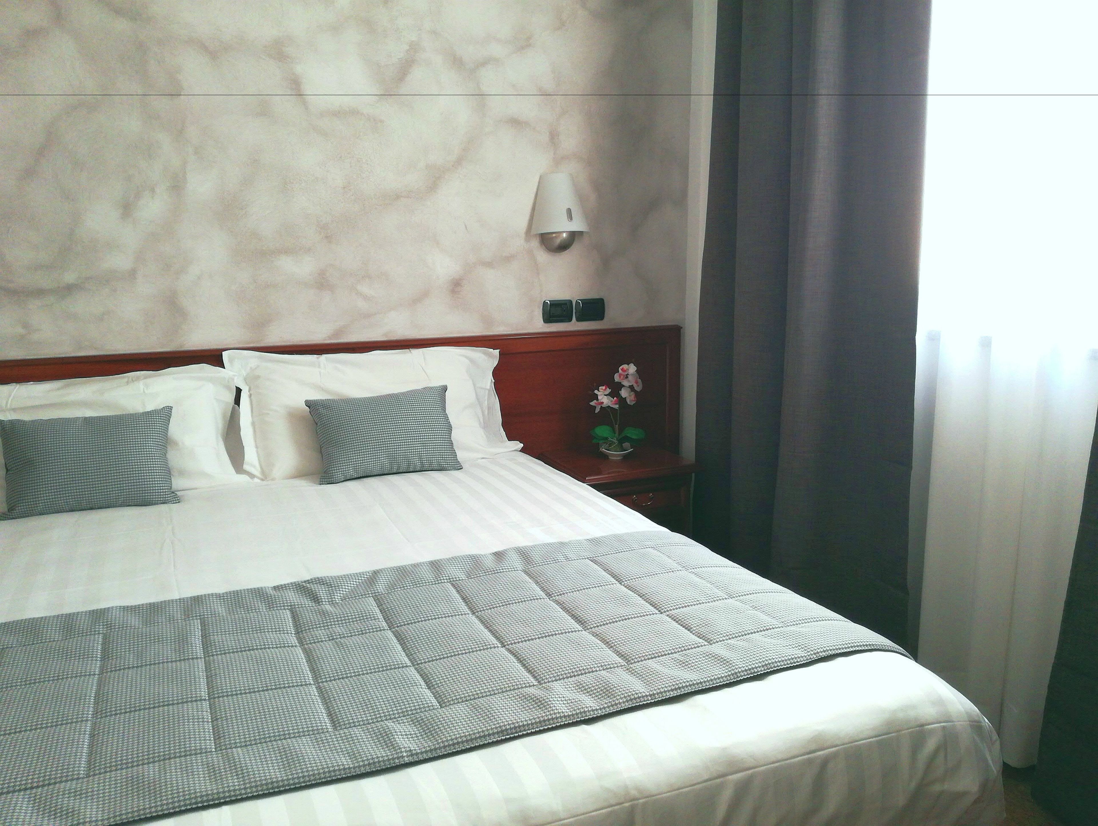 Una cama bien hecha con colcha a cuadros, cabecera de madera y mesita de noche con un florero.