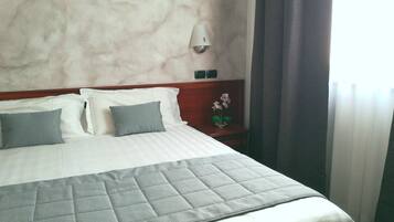 Una cama bien hecha con colcha a cuadros, cabecera de madera y mesita de noche con un florero.